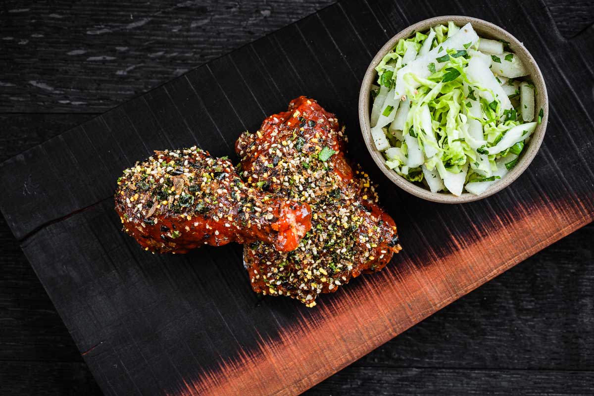 Cherry board with 2 pieces of fried chicken on the bone with gochujang sauce. Served with fresh Asian pear and cabbage slaw