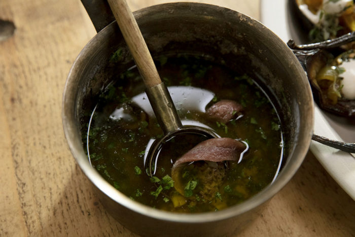 Bagna cauda with Italian parsley and floating Spanish anchovy in a saucepan.